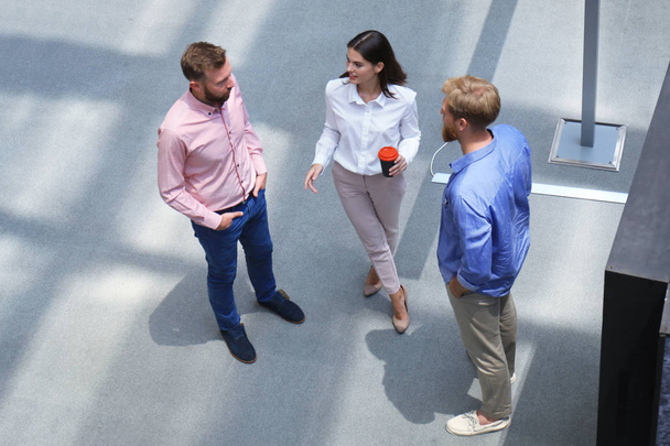 Vista superior de la gente joven moderna en ropa casual inteligente discutiendo negocios mientras está de pie en la oficina creativa
. - Foto, Imagen