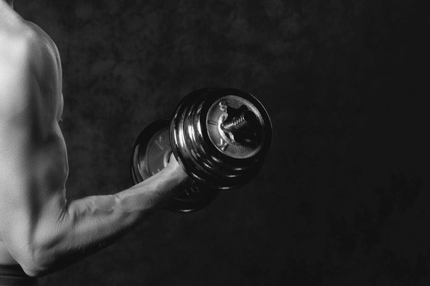 Part of mans body with metal dumbbell on a dark background - Photo, Image