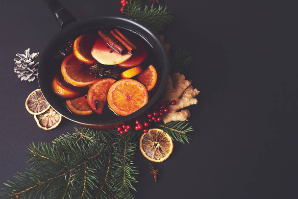Mulled wine in saucepan  with spices and ingredients on black background. Top view, flat lay. - Photo, image