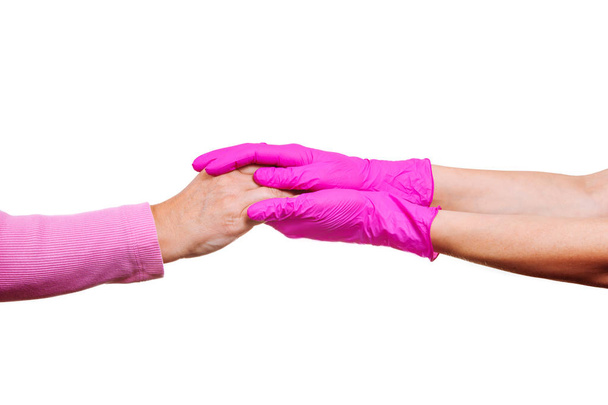 As mãos femininas de uma enfermeira ou médico em luvas médicas cor-de-rosa seguram as mãos de uma mulher idosa. Conceito de cuidado e apoio em hospício
. - Foto, Imagem