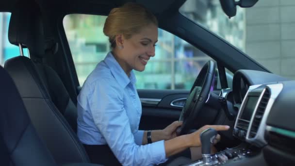 Naive blonde delighted with new car, touches random buttons, joyful as child - Filmati, video