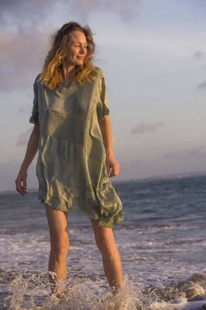 young happy and beautiful blond woman having fun at the beach in chic fashion dress playing with the sea feeling joyful and carefree in summer holidays travel and beauty concept - Photo, image