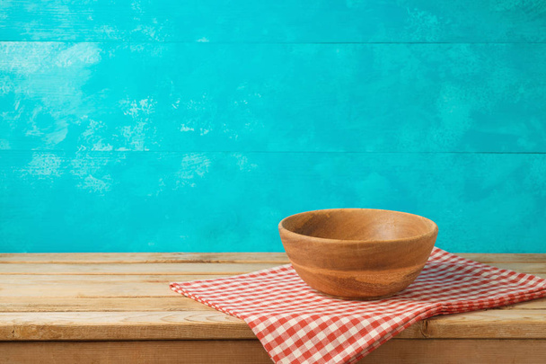 Empty wooden bowl on kitchen table with tablecloth over blue background - Foto, immagini