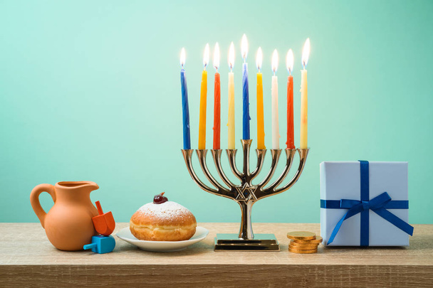 Jewish holiday Hanukkah background with menorah, sufganiyot, gift box and spinning tops on wooden table - Фото, зображення