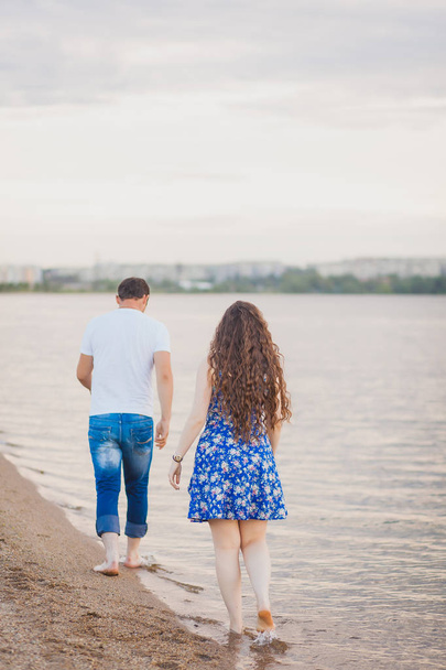 Back view of loving couple walking away with footprints at sandy beach. Girl with long curly hair - Фото, изображение