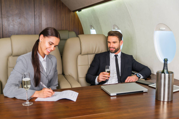 Businessman and woman working while travelling on private jet - Portrait of business people taking a first class flight for work, concepts about business and mobility - Photo, image