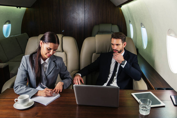 Businessman and woman working while travelling on private jet - Portrait of business people taking a first class flight for work, concepts about business and mobility - Foto, imagen