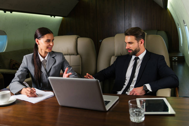 Businessman and woman working while travelling on private jet - Portrait of business people taking a first class flight for work, concepts about business and mobility - Foto, Imagen
