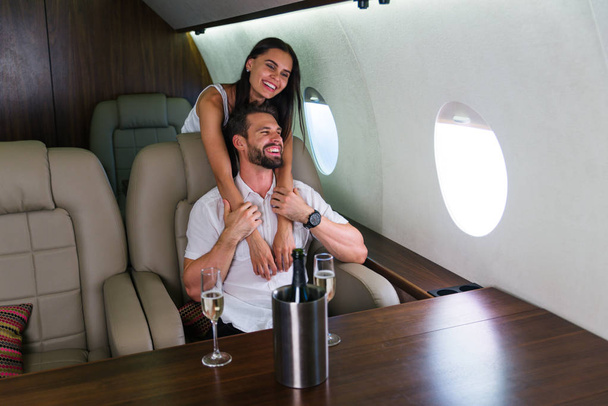 Pareja feliz viajando en un jet privado de lujo - Los adultos jóvenes viajan en un vuelo de primera clase, conceptos sobre viajes y estilo de vida
 - Foto, imagen