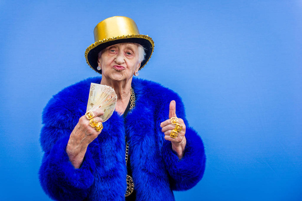 Funny and extravagant senior woman posing on colored background - Youthful old woman in the sixties having fun and partying - Фото, изображение