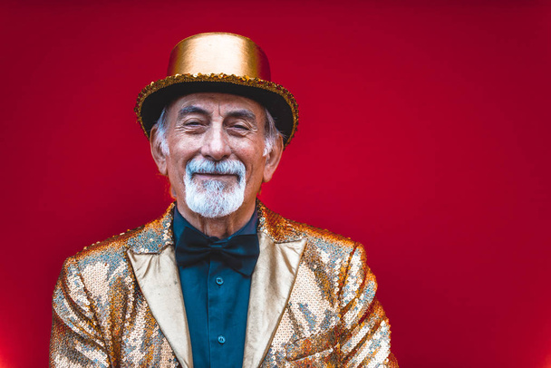 Funny and extravagant senior man posing on colored background - Youthful old man in the sixties having fun and partying - Фото, изображение