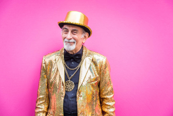 Funny and extravagant senior man posing on colored background - Youthful old man in the sixties having fun and partying - 写真・画像