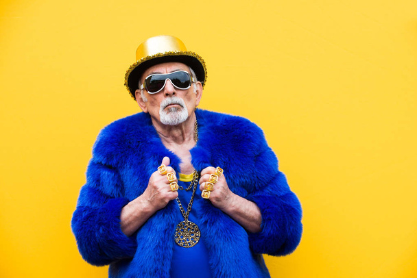 Funny and extravagant senior man posing on colored background - Youthful old man in the sixties having fun and partying - Photo, image
