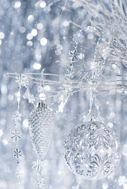 Błyszczące srebrne ozdoby świąteczne, wiszące na drzewie, z rozmyte Boże Narodzenie światła w tle. - Zdjęcie, obraz