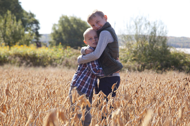 Two blond brothers hugging outside in a field on a sunny autumn day  - Foto, afbeelding