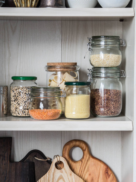 Shelf in the kitchen with various jars of cereals and kitchen chopping boards. Glass jars with pasta, lentils, couscous, beans and quinoa. - Foto, immagini