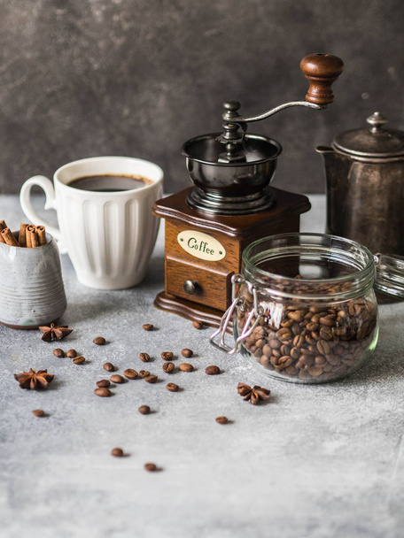 Various ingredients for making coffee, Glass jar with coffee beans, sugar, vintage coffeepot, coffee grinder, cup with coffee and milkman with cinnamon and anise stars on gray background. - Photo, image