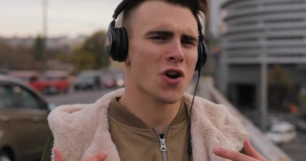 Young man enjoying listening to music with headphones dancing in city - Кадри, відео