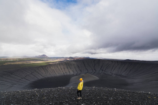 Jeune femme en imperméable jaune debout dans le cratère du volcan Hverfjall dans la région de Myvatn, Islande
. - Photo, image