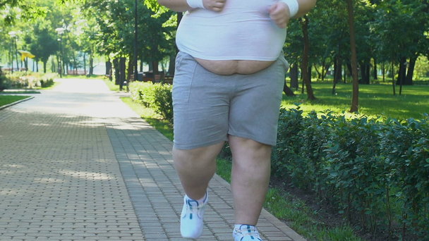 Fat man with big belly running in park early in morning, desire to lose weight - Кадры, видео