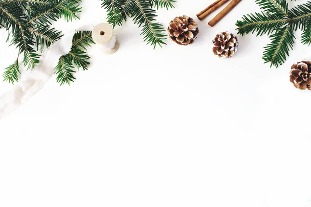Christmas festive styled stock composition. Fir tree branches border. Pine cones, cinnamon and silk ribbon on white wooden background. Flat lay, top view. Copy space. Decorative floral web banner. - Fotoğraf, Görsel