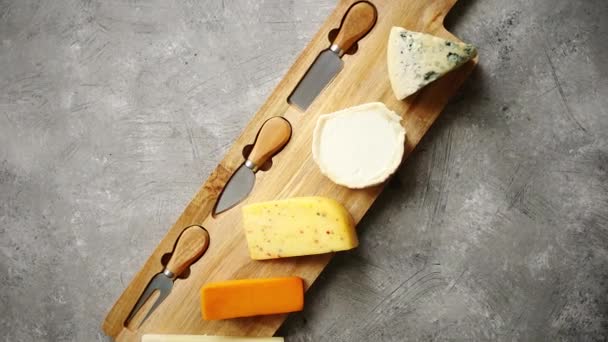 Assortment of various kinds of cheeses served on wooden board with fork and knives - Footage, Video