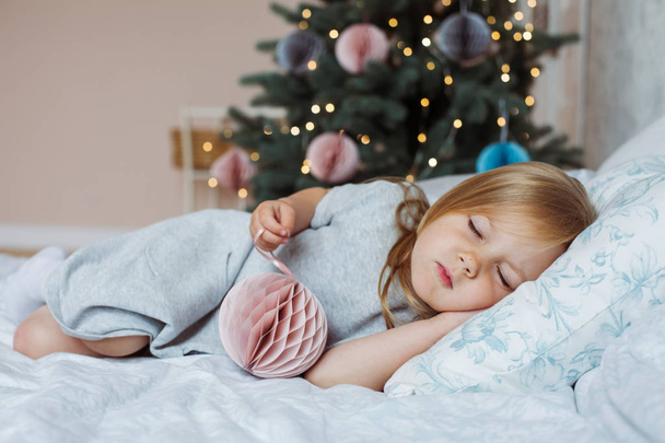 Kleines Mädchen schläft mit einem Spielzeug aus dem Haus am Weihnachtsbaum - Foto, Bild