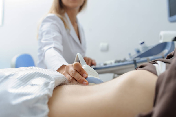 La doctora examina a un hombre en el abdomen con un dispositivo de ultrasonografía - Foto, imagen