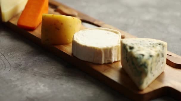 Ассортимент различных видов сыров, подаваемых на деревянной доске с вилкой и ножами - Кадры, видео