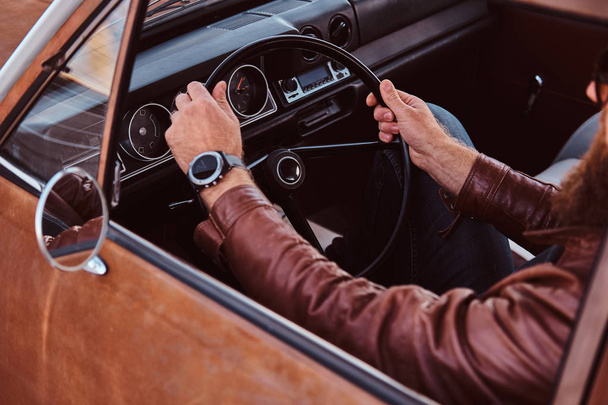 Bearded male in sunglasses dressed in brown leather jacket driving a retro car. - Foto, Imagem