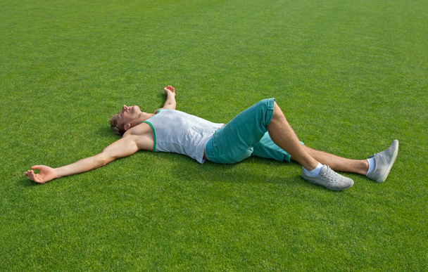 Спортивный парень отдыхает на зеленой тренировочной площадке
 - Фото, изображение