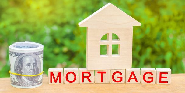 Miniature house and money. Wooden blocks and the inscription "mortgage". credit for property / apartment. Business loans for real estate concept. mortgage insurance - 写真・画像