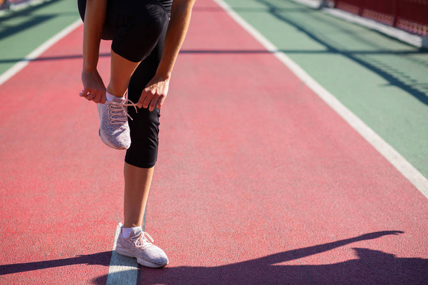 Giovane donna atletica allacciatura lacci di scarpe allo stadio in serata di sole. Spazio per testo
 - Foto, immagini