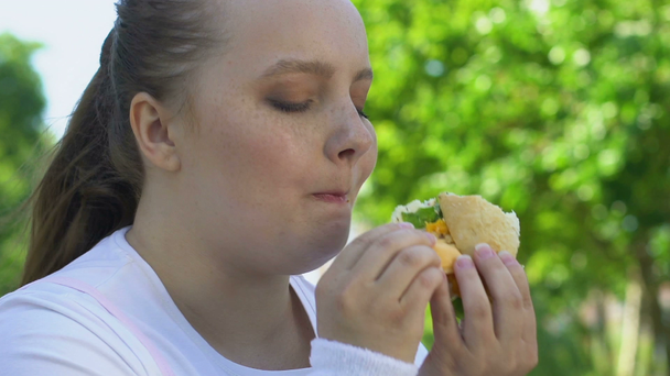 Dziewczyna jedzenia tłustych wysokiej kaloryczności burger, uzależnienie od jedzenia fast, brak silnej woli - Materiał filmowy, wideo