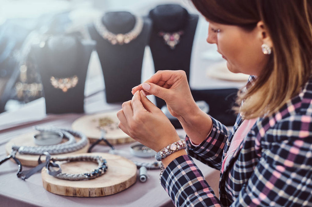 elegant gekleidete Frau fertigt handgefertigte Halsketten, arbeitet in der Werkstatt mit Nadeln und Faden. - Foto, Bild