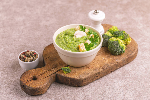 Fresh tasty pureed broccoli soup in clay bowl with ingredients on cutting board. Healthy food concept. Gray marble background. Horizontal view. Copy space - Valokuva, kuva