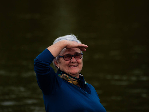 Una mujer mayor haciendo gestos y sonriendo en la orilla del río
 - Foto, Imagen