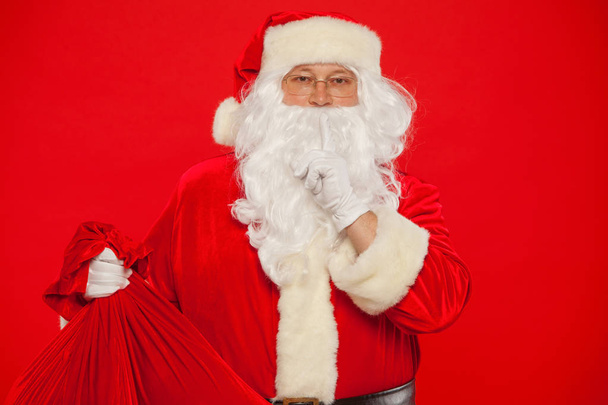 Christmas. Portrait of Santa Claus with huge red sack keeping forefinger by - Foto, afbeelding