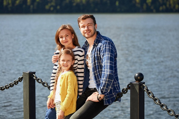 Happy Family looking at camera while posing on pier at quiet lake - Φωτογραφία, εικόνα