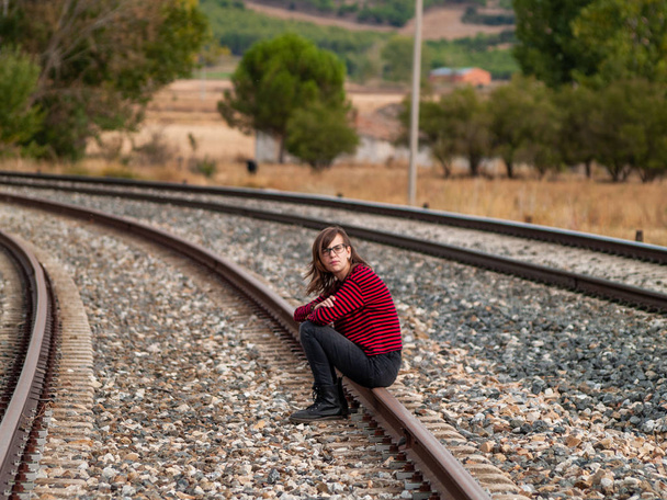 A lonely teen girl sitting on the train tracks - Foto, Imagen