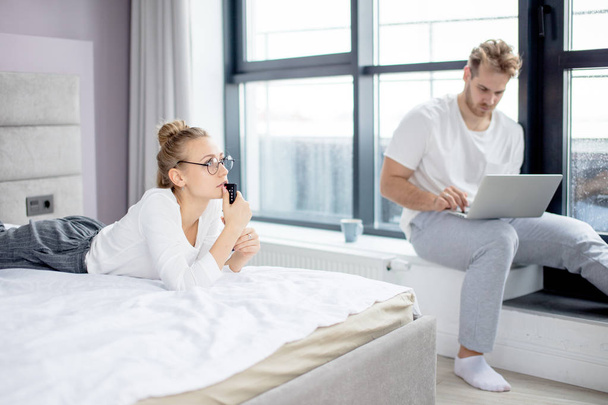 serious blond woman staring at TV while her boyfriend is sending e-mail - Foto, Bild