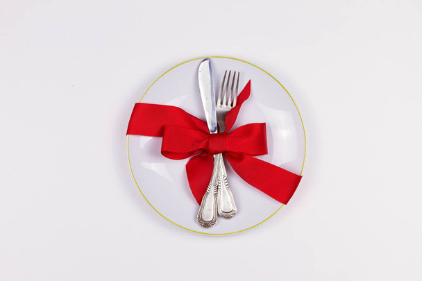 Christmas composition with plate, cutlery, pine branches, ribbon and red berries on white table. Winter holidays and festive background. Christmas eve dinner, New Year food lunch.  top view - Photo, image