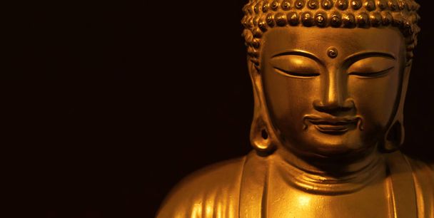 Golden Buddha statuette in the act of meditating (on black background with copy space) - Photo, Image