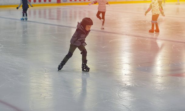 Adorabile bambino in abiti invernali con protezioni pattinaggio su pista di ghiaccio
 - Foto, immagini