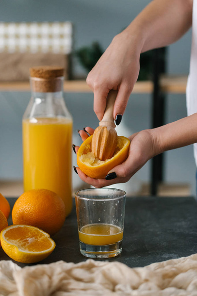 γυναίκα στα χέρια στύψιμο φρέσκο χυμό πορτοκαλιού, σε ποτήρι για πρωινό  - Φωτογραφία, εικόνα