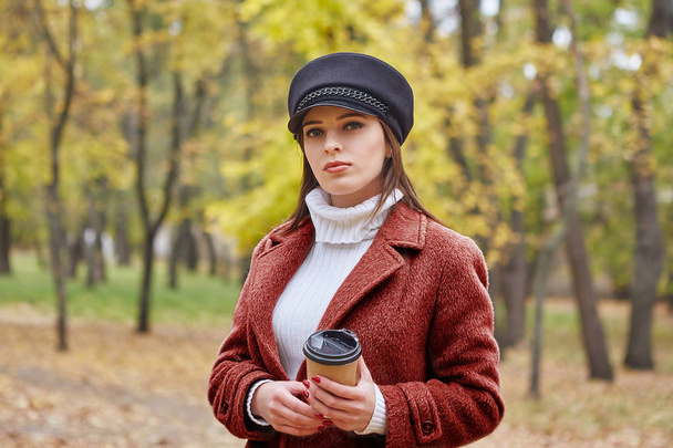 Beautiful woman in the autumn park enjoys good weather, coffee and silence - Photo, Image