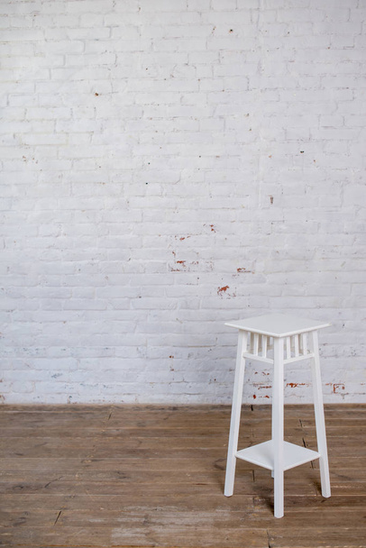 Bílá barová stolička na dřevěné podlaze proti bílé cihlové zdi. - Fotografie, Obrázek