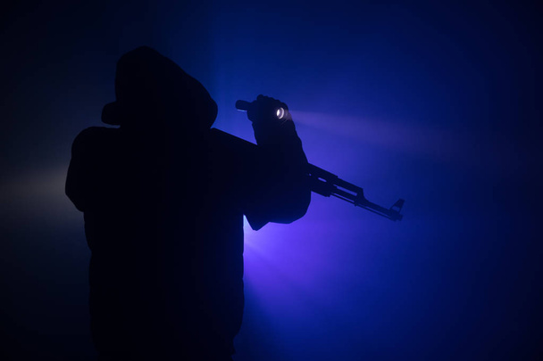 Σιλουέτα του ανθρώπου με την επίθεση τουφέκι έτοιμος να επιτεθεί σε σκούρο φόντο τονισμένο ομίχλη ή επικίνδυνο ληστή κρατώντας όπλο στο χέρι. Γυρίσματα τρομοκράτης με το όπλο θέμα ντεκόρ - Φωτογραφία, εικόνα