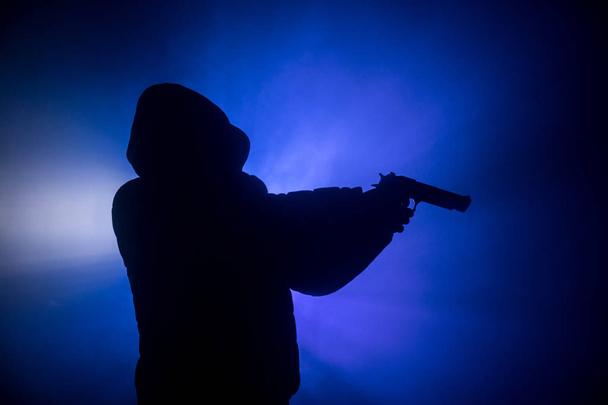 Силуэт человека с пистолетом, готового атаковать на темном туманном фоне или опасного бандита с пистолетом в руке. Стрельба в террориста с использованием темы оружия
 - Фото, изображение