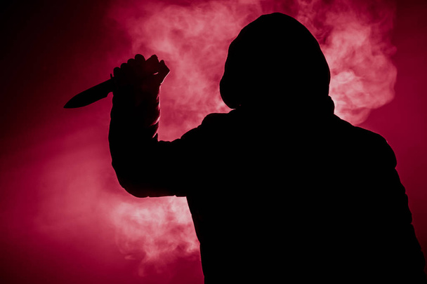 Опасный человек в капюшоне, стоящий в темноте и держащий нож. Лицо не видно. Совершение преступления
 - Фото, изображение